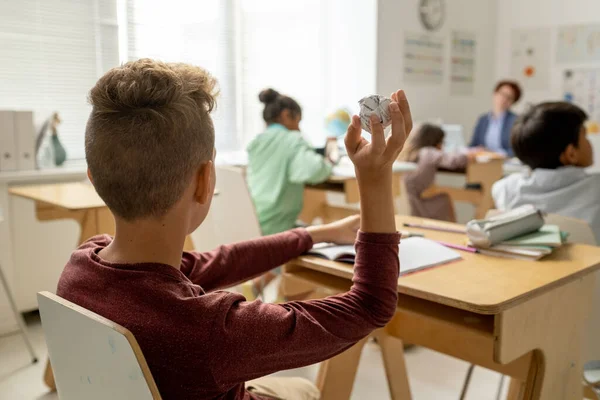 SChoolboy sosteniendo papel aplastado en la mano mientras está sentado junto al escritorio — Foto de Stock