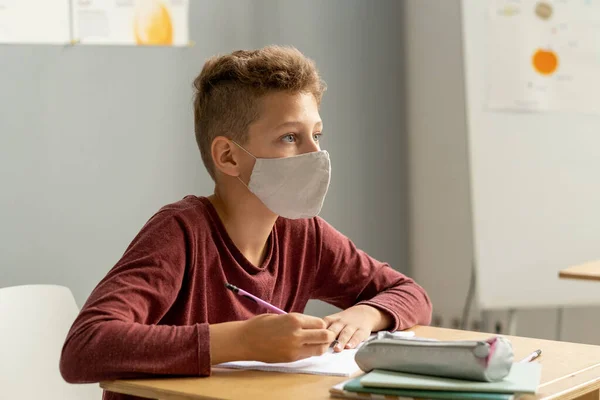 Симпатичный школьник в защитной маске смотрит на доску — стоковое фото