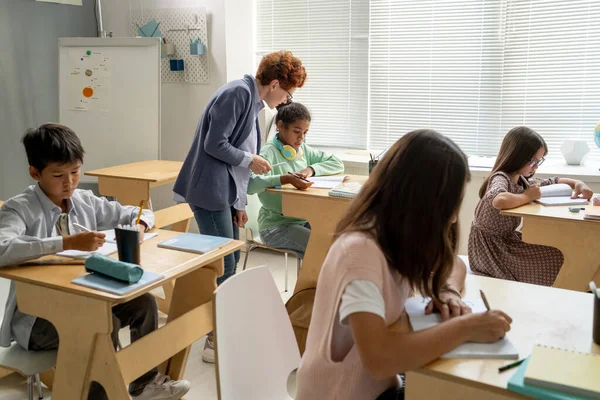 Youg profesor de pie por colegiala africana durante el trabajo individual —  Fotos de Stock