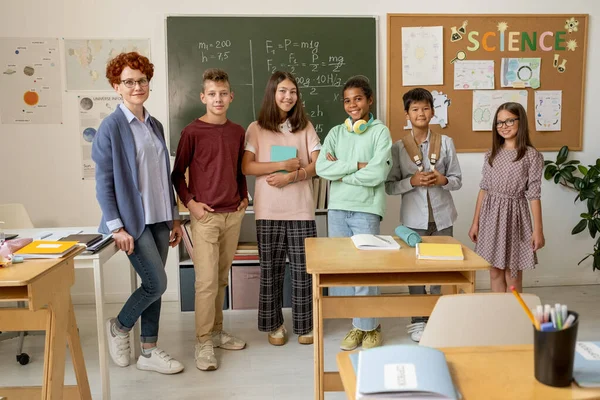 Giovane insegnante di successo e gruppo dei suoi studenti in piedi contro lavagne — Foto Stock