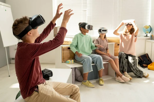 Schoolboy with ve headset touching large display during virtual presentation