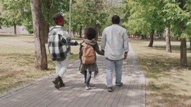 Modern Afro-Amerikalı çiftin ve oğullarının güneşli bir günde parkta birlikte yürüdükleri uzun bir arka plan çekimi.