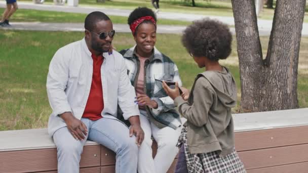 스마트폰을 귀엽고 아프리카 미국인 소년의 느림보 사진밝은 부모가 벤치에 사진을 — 비디오