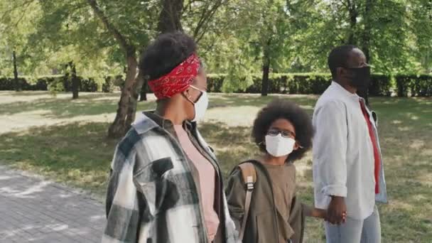 在温暖的阳光明媚的日子里 现代非洲裔美国人夫妇和他们可爱的儿子带着面具沿着公园散步聊天时的慢镜头 — 图库视频影像