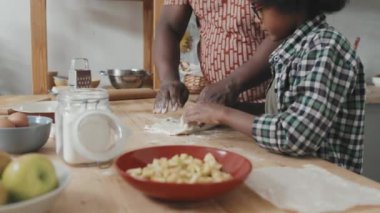 Yavaş çekimde Afro-Amerikalı bir adam ve küçük tatlı oğlu modern mutfakta elmalı turta yapıyor ve birlikte eğleniyorlar.