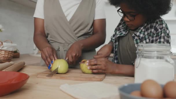 非洲裔美国母亲和她的小儿子一边切苹果 一边站在厨房桌子旁舒舒服服地吃着苹果派 他们的动作十分缓慢 — 图库视频影像