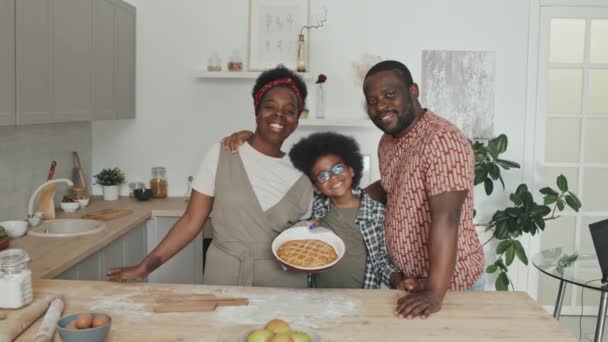 中低速ポルノの幸せなアフリカ系アメリカ人の家族の3つのポージングのためにカメラスタンドで現代的なキッチン 女性を保持おいしい自家製アップルパイ — ストック動画