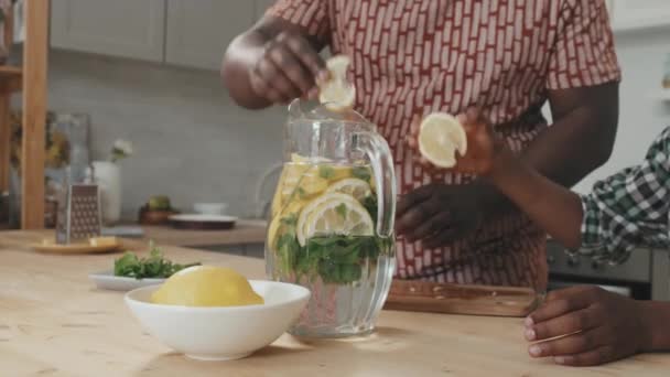 非洲裔美国人的父亲和儿子在家里做新鲜柠檬水 在罐子里加柠檬片 — 图库视频影像