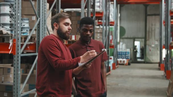 带剪贴板的白人年轻人和他的非裔美国男同事在五金店仓库检查库存的慢速跟踪 — 图库视频影像