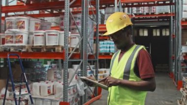 Ağır çekimde, hırdavatçı dükkanında tablet kullanan siyah şapkalı ve güvenlik yeleği giyen Afro-Amerikan erkek işçilerin portresi.