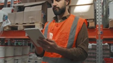 Yansıtıcı turuncu yelek ve ambardaki tableti kullanarak ağır ağır çalışan erkek işçilerle el kamerasını yukarı kaldır.