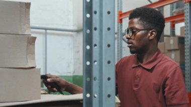 Barkod okuyucu kullanan ve nalbur deposundaki karton kutuları kontrol eden gözlüklü Afro-Amerikan bir adamla el bilgisayarı takibi