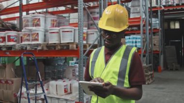 Afro-Amerikan erkek işçilerin yansıtıcı yelek ve sert şapka giyip hırdavatçıdaki depoda tablet kullandıkları el kameraları yavaş çekimde çekildi.