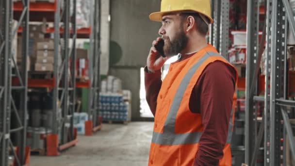 Sakallı Güvenlik Yeleği Kasketli Bir Adamın Depoda Cep Telefonuyla Konuşmasının — Stok video