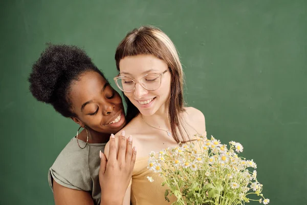 Feliz mujer africana abrazando a su novia con ramo de flores silvestres — Foto de Stock