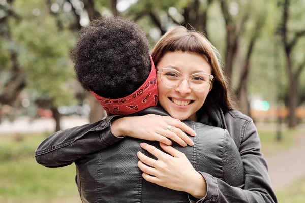 Chica feliz mirándote mientras abraza a su novia africana al aire libre — Foto de Stock