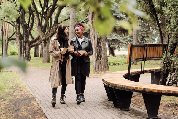 Dos amorosas novias interculturales con snacks paseando por el parque — Foto de Stock
