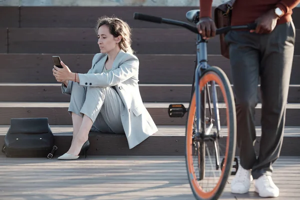 Allvarlig affärskvinna sms i smartphone med mannen driver cykel framför — Stockfoto