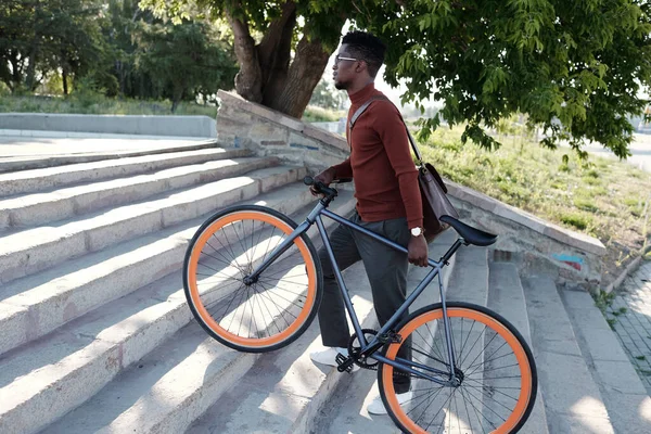 Yukarı çıkarken bisikletle gezen genç Afrikalı işadamının yan görünüşü — Stok fotoğraf