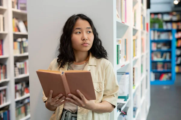 Ung asiatisk kvinna håller öppen bok i biblioteket — Stockfoto