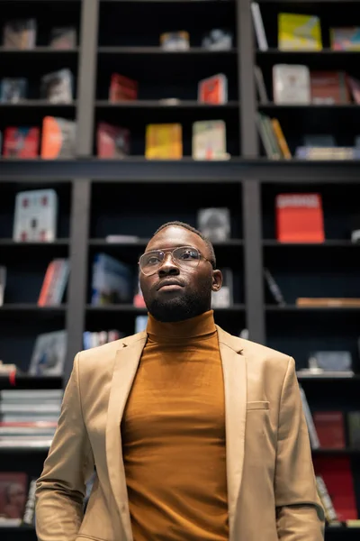 Fiatal afro-amerikai férfi okos alkalmi viseletben, nagy könyvesboltban áll — Stock Fotó