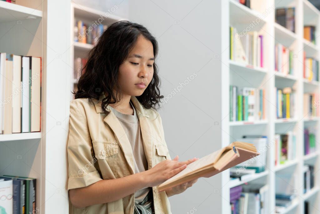 Serious female student with open book reading text