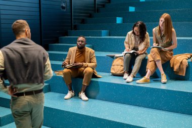 Akıllı günlük giyimli çalışkan öğrenciler seminerde koça bakıyorlar.