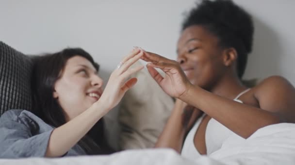 中出しの遅いですの多民族愛レズビアンカップル嘘でベッドと絡み合い指に笑顔でお互いにチャット — ストック動画