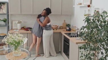 Çok ırklı mutlu lezbiyen çiftin, kahvaltı hazırlarken sohbet ve kucaklaşmalarının orta ölçekli bir resmi.