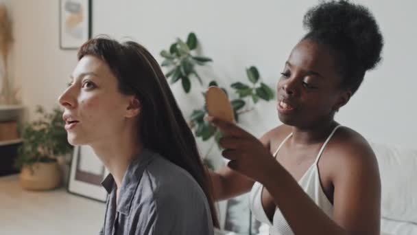 手持跟踪器 慢吞吞地微笑着的非洲裔美国女人梳理着她的白人女友的头发 — 图库视频影像