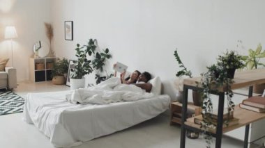 Homoseksüel bir çiftin rahat bir dairede yatakta uzanıp tablet kullanmasıyla elde tutulan izler.