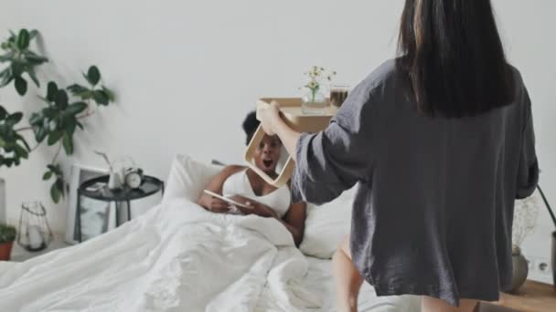 慢速跟踪带着托盘的年轻女子进入舒适的卧室 她在床上吃早饭使女朋友大吃一惊 — 图库视频影像