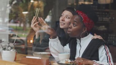 Kafe 'nin mutlu Kafkasyalı ve Afro-Amerikalı kız arkadaşlarının penceresinden el kamerasıyla çekilen yavaş çekim. Pencereden dışarı bakarken yemeğin ve sohbetin tadını çıkarıyor.