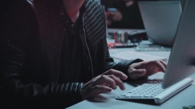 Ceketli ve şapkalı genç erkek hacker 'ın el kamerasıyla çekilmiş görüntüsü. Masada oturuyor ve bilgisayarda saklanıyor.