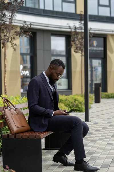 Hombre de negocios africano serio en traje de desplazamiento en el teléfono inteligente —  Fotos de Stock