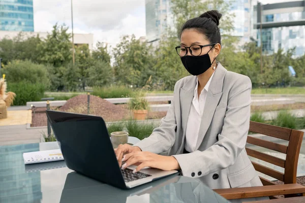 Jovem elegante mulher de negócios asiática digitando no teclado do laptop em ambiente urbano — Fotografia de Stock