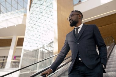 Takım elbiseli genç işadamı aşağı doğru yürürken yürüyen merdivende duruyor.