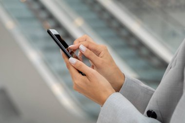 Takım elbiseli genç bir kadının elleri kameranın önünde cep telefonuyla kayıyor.