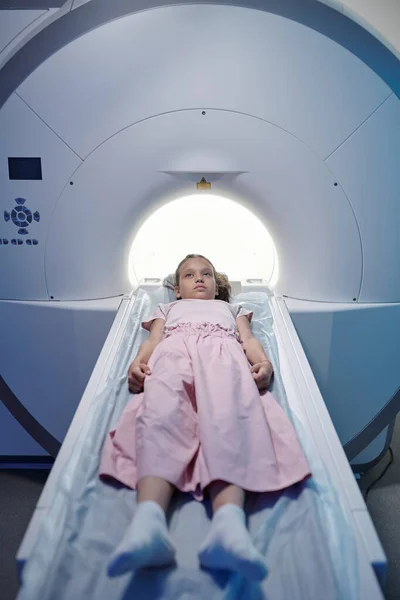 Kislány fekszik a hosszú orvosi asztalon, és beköltözik az MRI szkennelő gépbe. — Stock Fotó