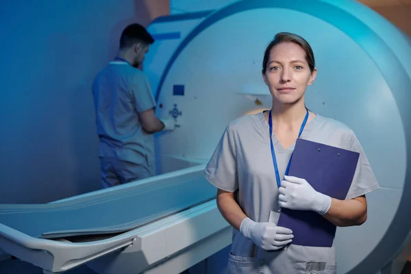 Jovem enfermeira de uniforme e luvas em pé na frente da máquina médica — Fotografia de Stock