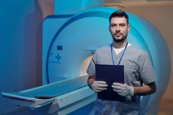 Young successful radiographer with document standing against medical equipment — Stock Photo, Image