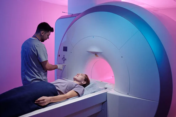 Jovem médico pressionando o botão no painel para iniciar o procedimento de ressonância magnética — Fotografia de Stock