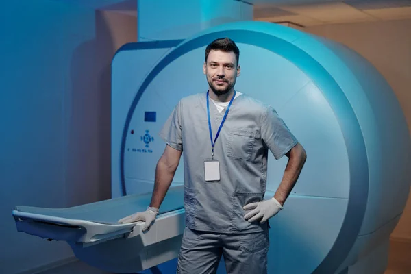 Självsäker läkare i grå uniform stående vid bordet med MRI-avsökningsutrustning — Stockfoto