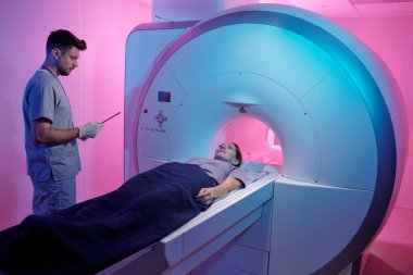 MRI makinesinin masasında havluyla kaplanmış genç bir hasta var.