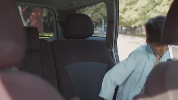 朝学校に行くか 親によって学校からピックアップされている間 バックパックが助手席に入り 彼のシートベルトを固定して車の中から手持ち撮影 — ストック動画