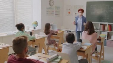 Bir grup ortaokul öğrencisine matematik öğreten yüz maskeli kadın öğretmenin el kamerasıyla çekilmiş fotoğrafı. Ayrıca salgın hastalığın ortasında okula döndükten sonra yüz maskesi takıyorlar.
