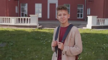 Okul binasının önünde sırt çantalı ve kameraya gülümseyen 13 yaşında bir çocuğun el yapımı portresi.