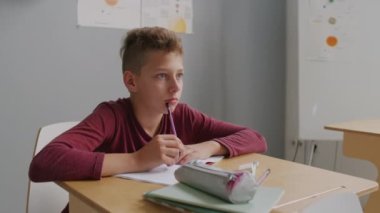 13 yaşındaki odaklanmış bir çocuğun el kamerasıyla derste otururken ve öğretmenini kamerasız dinlerken not defterine yazarken görüntüsü.