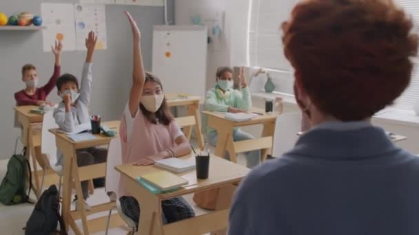 一组戴口罩的中学生坐在课桌前举手回答女教师的提问的手持照片 — 图库视频影像