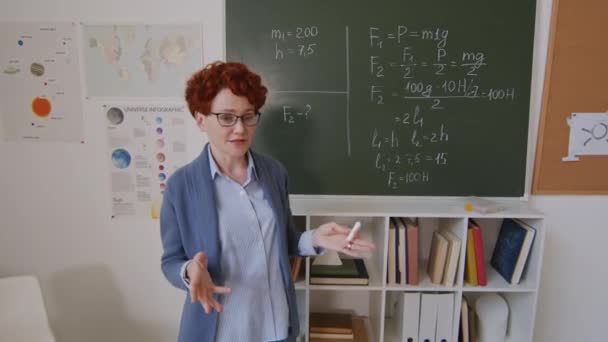 一个矮小的红头发女人站在黑板旁边 教一群坐在课桌旁的中学生数学 她在解释信息 孩子们举手 — 图库视频影像